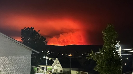 Hinter einem Haus brennt der Wald: der Himmel leucht rot