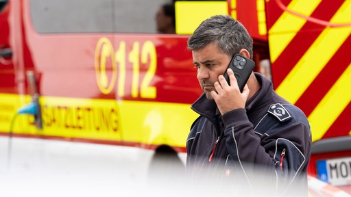 Feuerwehrmann steht vor Feuerwehrauto und telefoniert mit dem Handy
