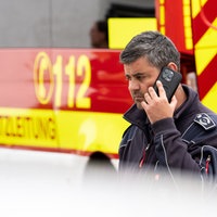 Feuerwehrmann steht vor Feuerwehrauto und telefoniert mit dem Handy