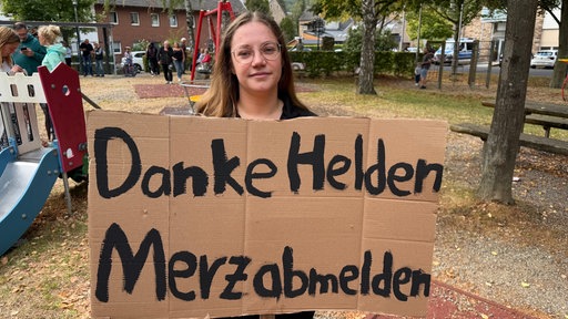 Eine Frau hält ein Plakat mit der Aufschrift "Danke Helden Merz abmelden".