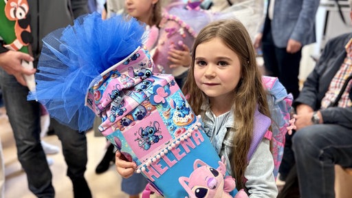 Helena hat ihre Schultüte im Arm und ihre Schultasche auf dem Rücken. 