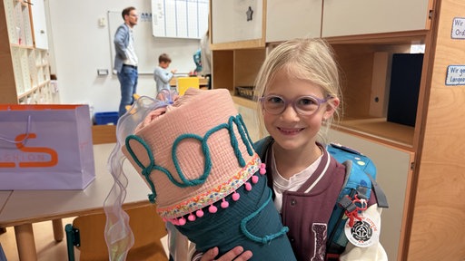 Romy trägt ihre Schultüte und ihre Schultasche.