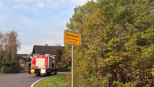 Ein Straßenschild mit der Aufschrift "Schmidt Stadt Nideggen Kreis Düren". Dahinter ist ein Feuerwehrauto.