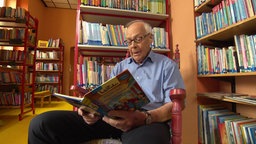 Ein Senior sitzt mit einem aufgeschlagenem Bilderbuch vor einem Bücherregal