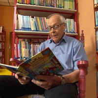 Ein Senior sitzt mit einem aufgeschlagenem Bilderbuch vor einem Bücherregal