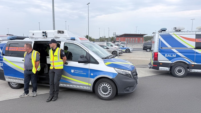 Zwei Männer in Warnwesten stehen vor einem offenen Traffic Control Sprinter auf einem Parkplatz