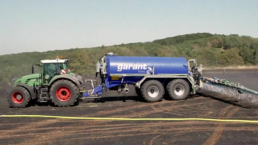 Ein Traktor, der einen Anhänger mit Wasser und eine Pflug über den Acker zieht.