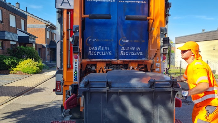 ein Müllwerker mit einem Sonnenschutz schiebt eine Mülltonne in Richtung Müllwagen