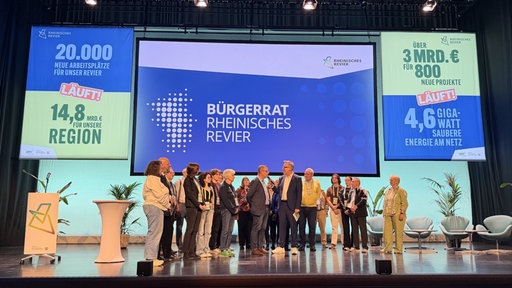 Teilnehmer der Revier-Konferenz in Bergheim stehen auf einer Bühne. 