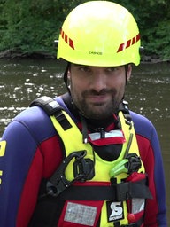 Strömungsretter Sebastian Plum steht mit neongelbem Helm und Neoprenanzug in der Rur