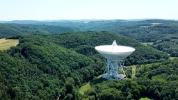 Das Radioteleskop aus der Ferne. Es steht zwischen Hügeln und Wäldern.