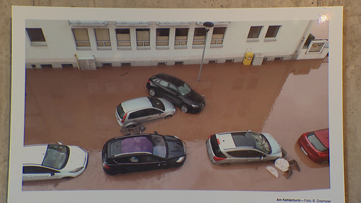 Mehrere überflutete Autos stehen in braunem Wasser in einer Wohngegend.