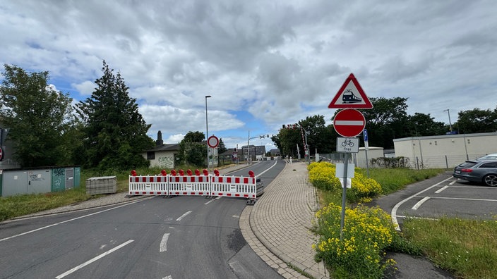 Eine abgesperrte Straße mit einem DUrchfahrt-Verboten-Schild. Im Hintergrund steht ein Bahnübergang. 