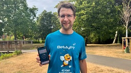 Ein Mann in Sportkleidung zeigt ein Handy mit einer App in die Kamera