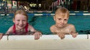 Zwei Kinder halten sich im Schwimmbad am Beckenrand fest