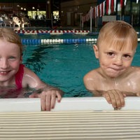 Zwei Kinder halten sich im Schwimmbad am Beckenrand fest