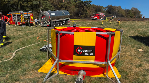 Mehrere Feuerwehr-Einsatzfahrzeuge auf einem Feld. Vorne im Bild ein gelb-roter faltbarer Wassertank