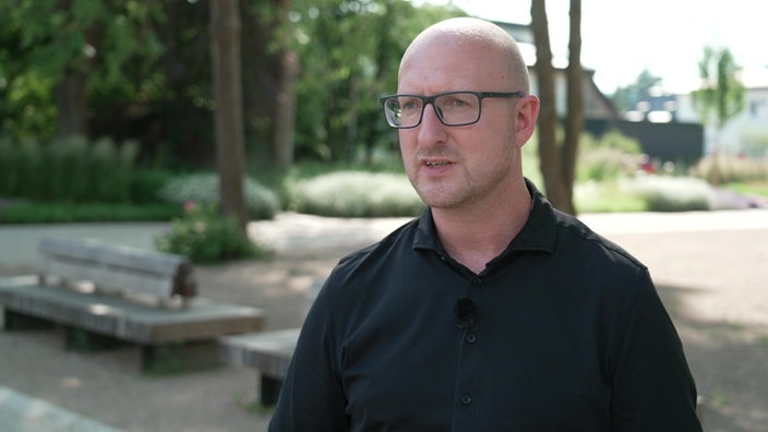 Ingo Pfennings, der Bürgermeister von Schleiden, steht in schwarzem T-Shirt in einem Garten vor Bäumen