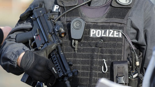 Polizist mit einer schusssicheren Weste hält ein Maschinengewehr in der Hand