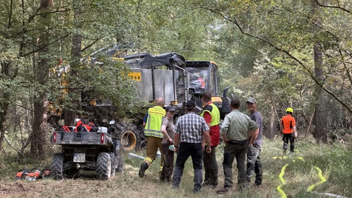 Ein großes Löschfahrzeug steht im Wald, umgeben von Einsatzkräften