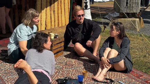 Besucher des Festivals sitzen auf einem Teppich in der Sonne