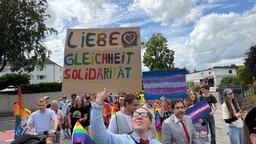 Parade Zug mit Plakaten. Im Vordergrund ein Plakat mit der Aufschrift "Liebe, Gleichheit, Solidarität".