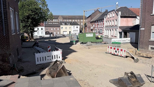 Eine große Baustelle mit Bauzäunen und aufgerissenem Asphalt umgeben von alten Häusern in Gangelt
