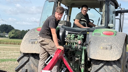Christoph Deckers und Marius Meyer sitzen auf einem Trecker und blicken nach hinten auf das Feld, auf dem sie arbeiten