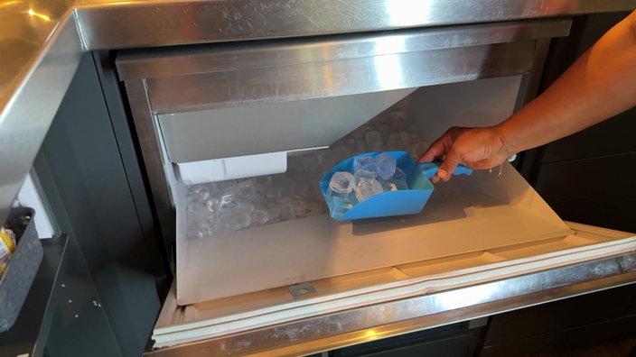 Eine Person, die mithilfe einer Schippe Eiswürfel aus einer Maschine nimmt.