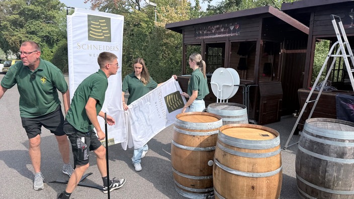 zwei Frauen und zwei Männer in grünen T-Shirts bauen eine Fahne vor einem Verkaufsstand auf 