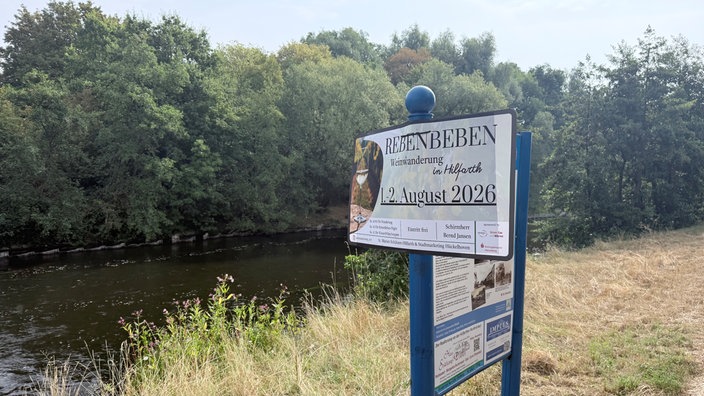 ein Schild auf einer Wiese an der Rur weist auf die anstehende Weinwanderung hin 