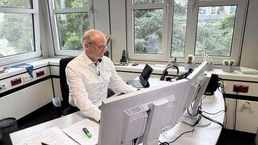 Christoph Breuer sitzt in einem Büro an seinem Arbeitsplatz. 