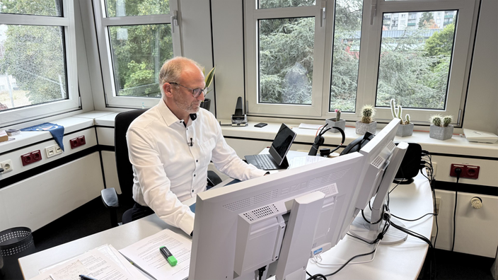 Christoph Breuer sitzt in einem Büro an seinem Arbeitsplatz. 