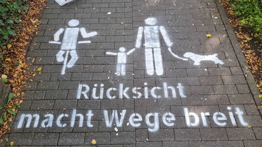 Eine Kreide-Markierung auf einem Fußgängerweg, zu lesen ist "Rücksicht macht Wege breit"