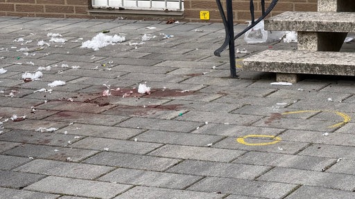 Eine Haus-Einfahrt, am Boden mit Blutflecken, Taschentücher und Markierungen der Polizei