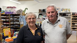 Ein Paar in Tshirts mit dem Tafel-Logo darauf steht Arm in Arm im Depot