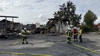 Fünf Feuerwehrleute stehen in Montur und mit Schläuchen vor dem abgebrannten Haus