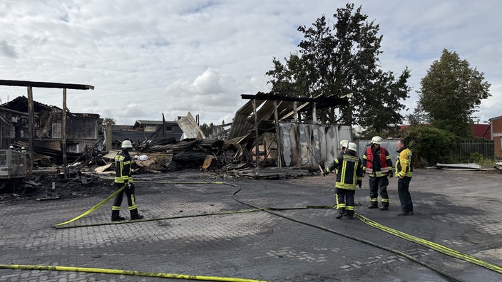 Fünf Feuerwehrleute stehen in Montur und mit Schläuchen vor dem abgebrannten Haus