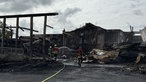 Einige Feuerwehrleute löschen in der abgebrannten Lagerhalle