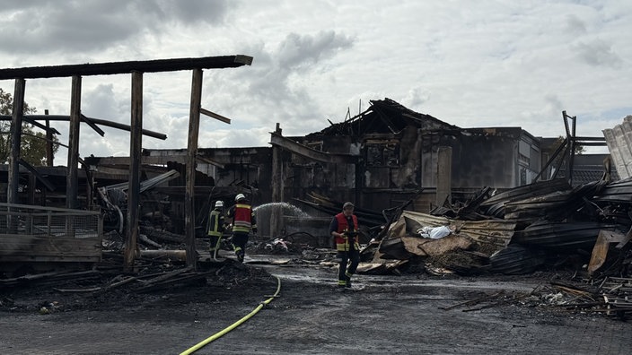 Einige Feuerwehrleute löschen in der abgebrannten Lagerhalle