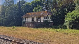 Das Bahnhäuschen in Wegberg ist an den Gleise gelegen. Es ist weiß und aus Fachwerk. An seiner Fassade rankt Efeu. 