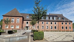 Das Wegbeger Rathaus ist aus Backsteinen und hat weiße Fensterrahmungen aus Stein. Auf dem Vorplatz stehen Bäume. 