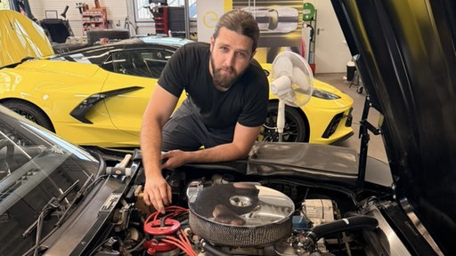 Lorans Omar hinter einer geöffneten Motorhaube in der Werkstatt