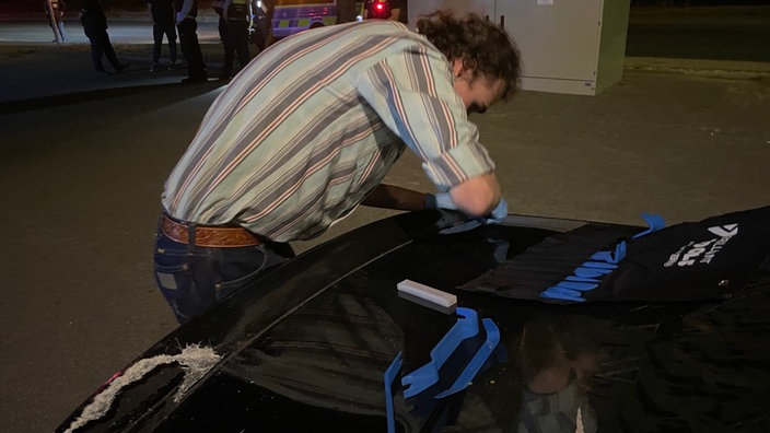 Ein Mann entfernt den illegal angeklebten Spoiler von seinem Auto