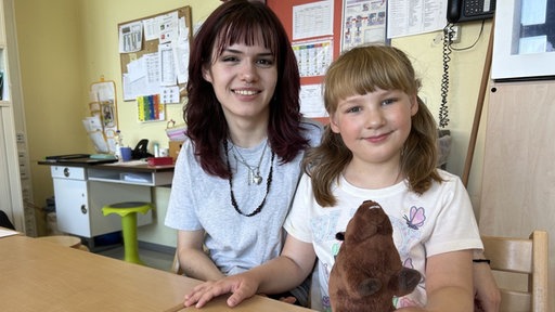 Praktikantin und Mädchen sitzen in Schule und lachen 