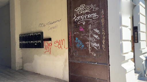 Ein Hauseingang mit mehrern Briefkästen. An der Wand befindet sich Graffiti