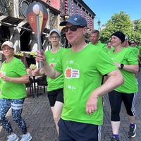 Mehrere Läufer in neongrünen T-Shirts laufen über den Marktplatz in Aachen. Der vorderste Läufer trägt eine unechte Fackel. 