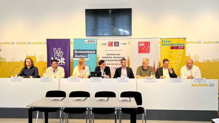 Politiker sitzen vor Aufstellern der vier Parteien an einem Tisch