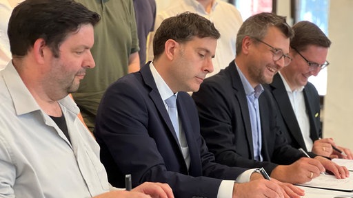 Politiker unterschreiben den Koalitionsvertrag an einem Tisch