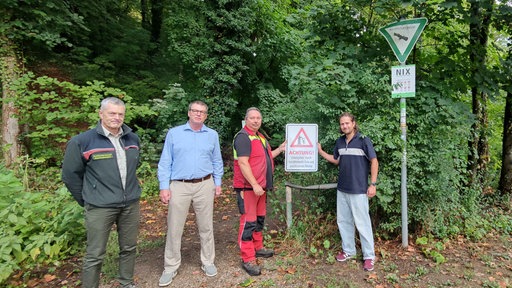 Das Bild zeigt vier Männer, die ein Warnschild vor dem Frankenwald hochhalten